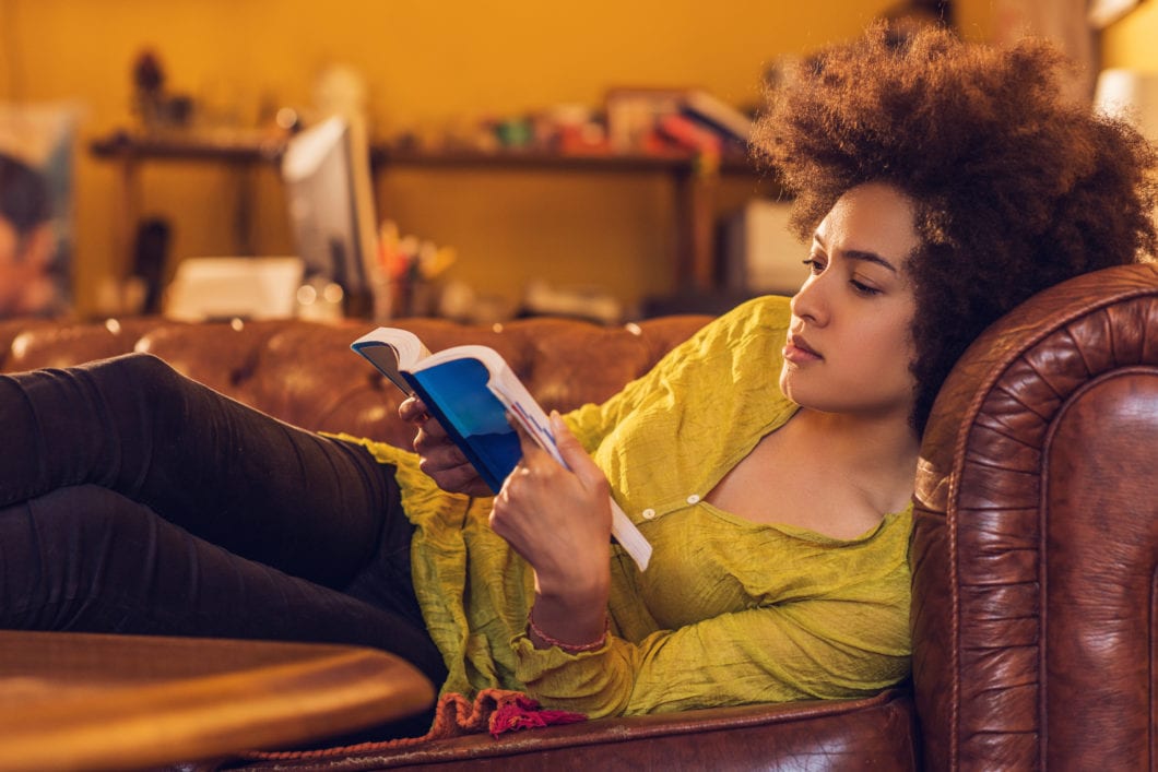 African American woman enjoying while reading a book at home ...