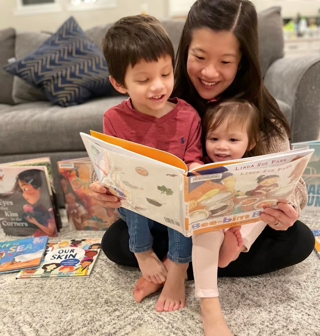 Community Voices Kit #1 cover image. A mom sits on the floor with two kids on her lap, reading the picture book "Bee-bim BOP!"