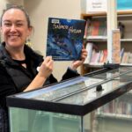Librarian holding book about salmon near fish tank