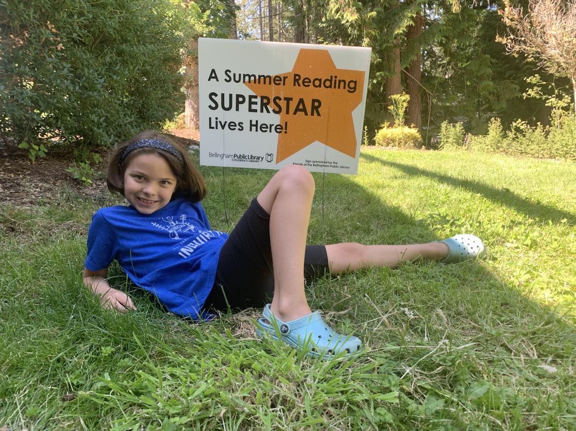 Child in front of a sign that says Summer Reading Superstar.