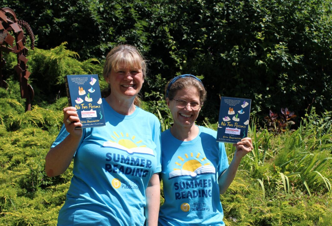 Two Library staff wearing Summer Reading T-shirts holding the book titled No Two Persons