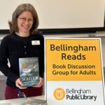 Librarian holding book near a sign for Bellingham Reads