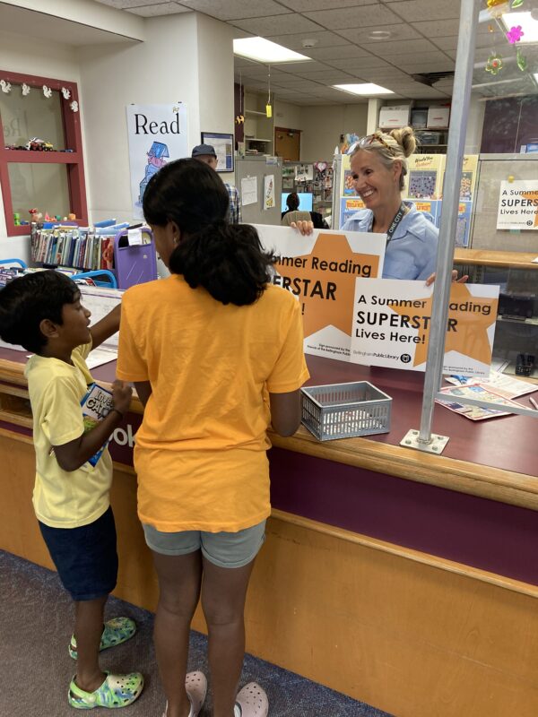 Bellingham Mayor Kim Lund giving a Summer Reading Superstar sign to two kids