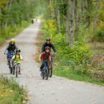 Adult and three kids biking on a gravel path