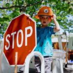 child wearing a hard hat holds a stop sign