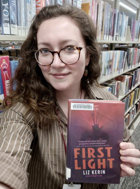 a person standing in front of bookshelves and holding up a single book
