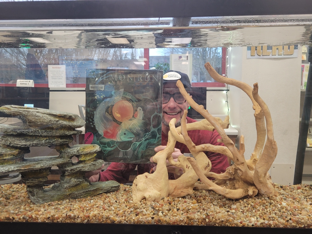 Library staff displaying a book about salmon through an aquarium