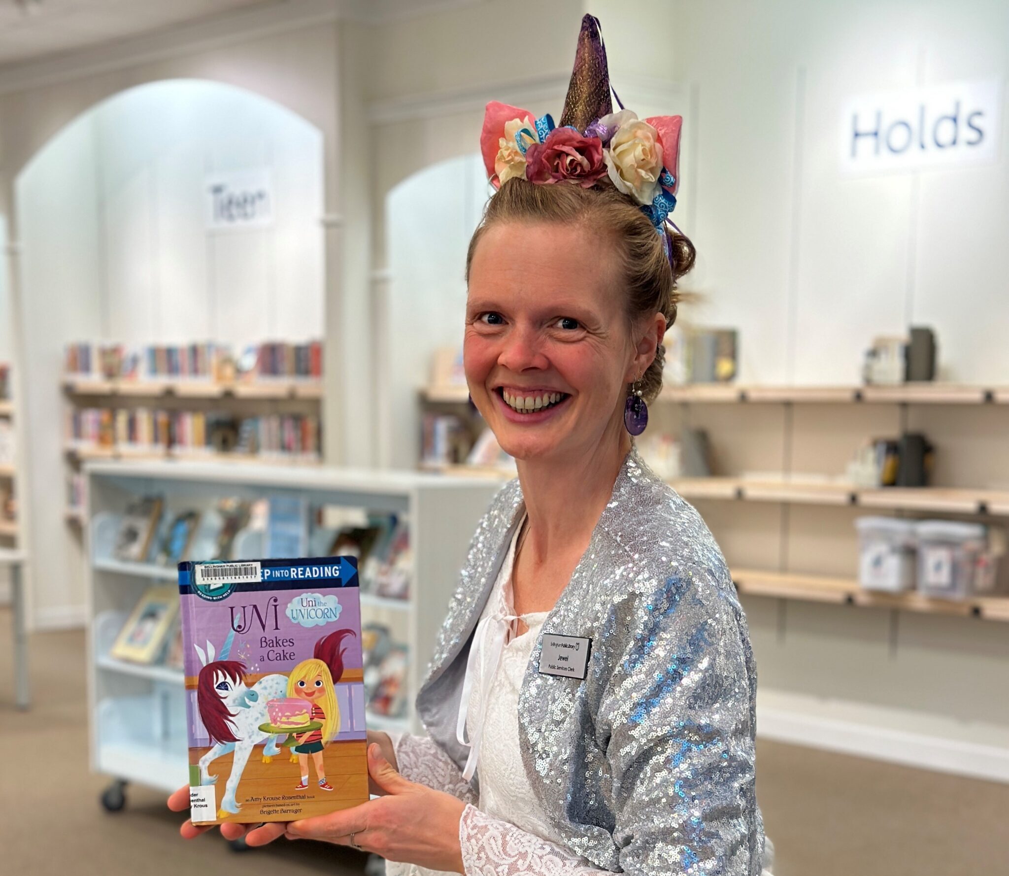 A woman in a unicorn costume holding up a children's book about unicorns