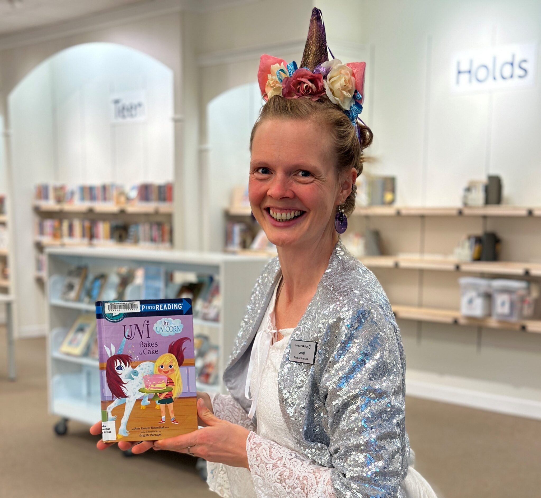 A woman in a unicorn costume holding up a children's book about unicorns