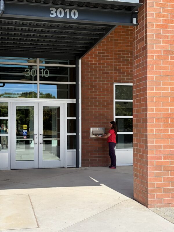 Person returning holds at outdoor book drop at BTC with address of building in view